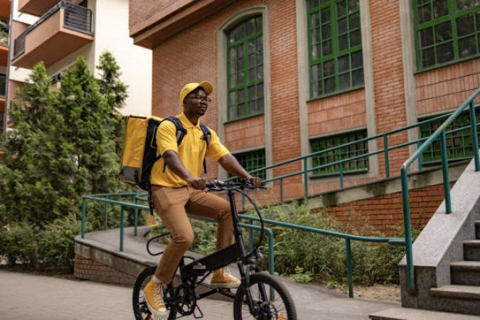 Young black courier cycling while delivering packages on the street.