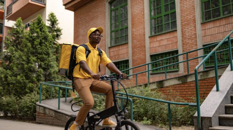 Young black courier cycling while delivering packages on the street.